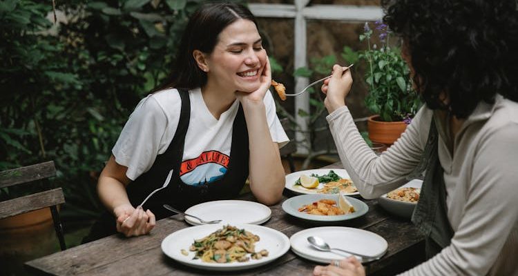 Two people enjoying a meal at an outdoor kitchen table, one feeding the other.